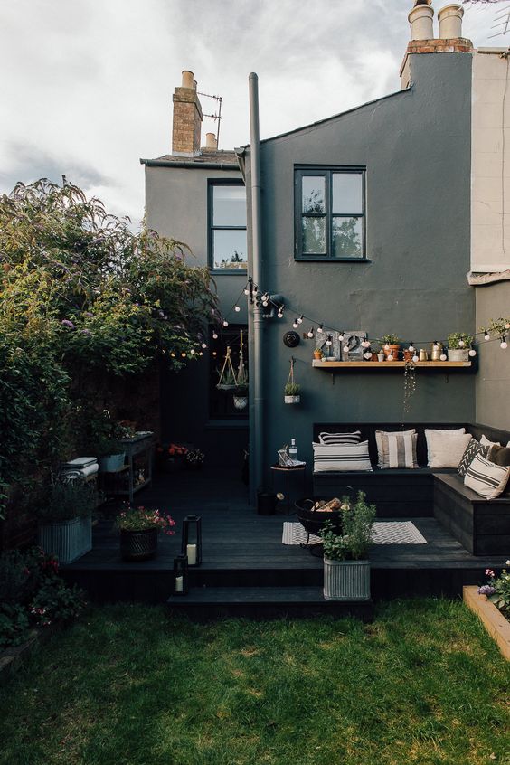 a small Scandinavian backyard with a black deck, a black corner bench, a green lawn and some blooms all around