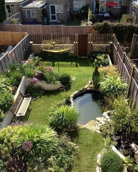 a small and cool backyard turned into a garden, with a pond, a green lawn, some blooms and plants and a bench
