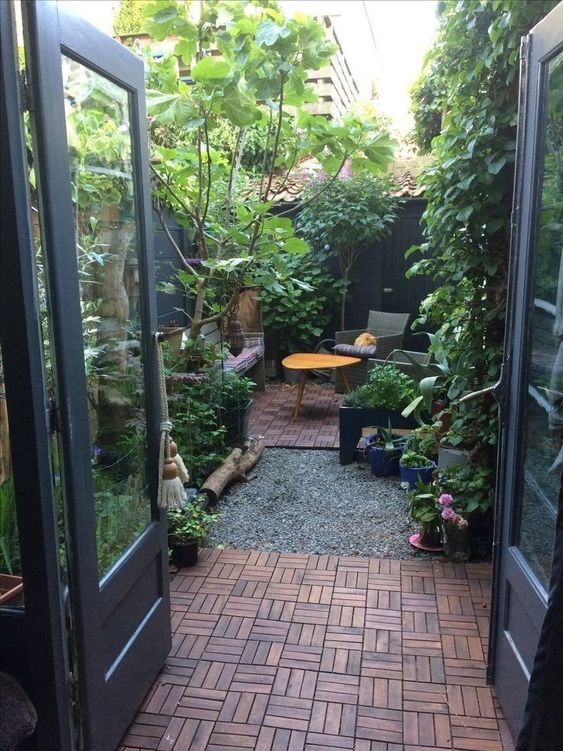 a small and cool courtyard to have a rest in, wiht a wooden deck, some simple outdoor furniture, greenery, trees and a living wall