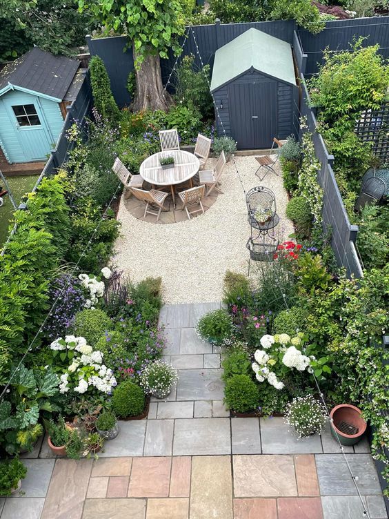 a small and lovely backyard with a dining space, lots of growing and potted greenery and blooms and string lights over the space