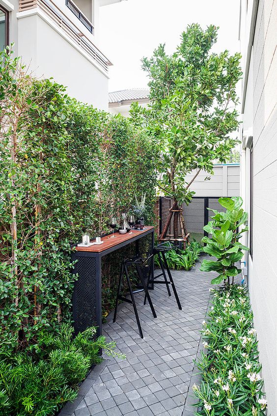 a small and lovely backyard with a living wall, some blooms, trees, a bar counter and tall stools is amazing