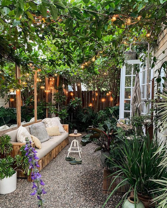 a small and welcoming backyard with a sofa, potted plants and blooms, climbing plants over the space and lights