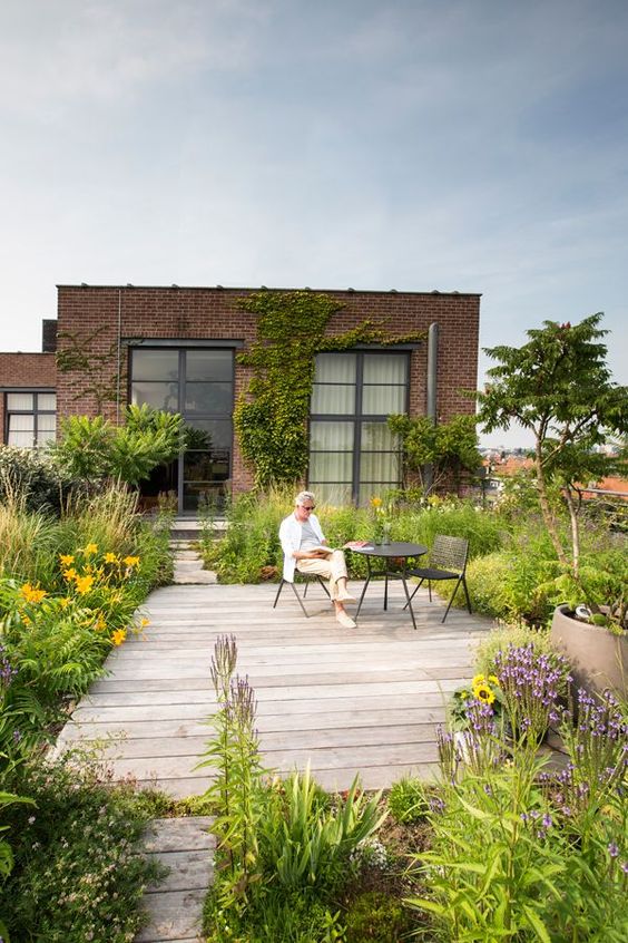 a small and welcoming backyard with lots of greenery and bright blooms, with a wooden deck and some simple furniture