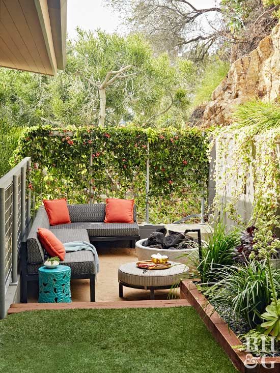 a small backyard with a sunken part with a corner sofa, a fire pit, an ottoman, greenery walls and a green lawn