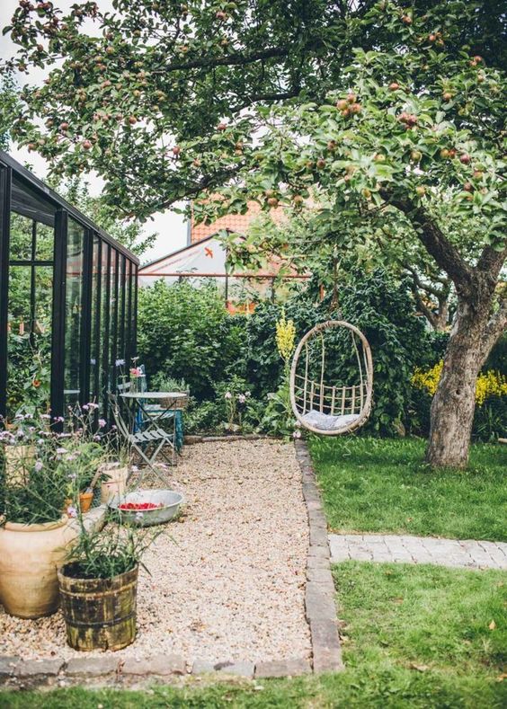 a small backyard with a suspended chair, some garden furniture, potted blooms and a green lawn