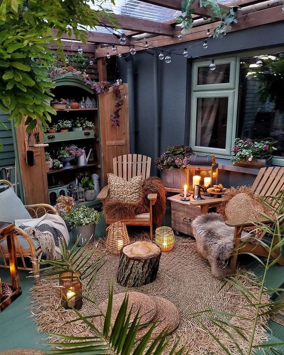 a small backyard with a wardrobe used as a plant stand, wooden and rattn chairs, candle lanterns, a tree stump and some jute rugs