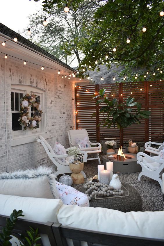a small eclectic backyard with a fire pit, some white vintage furniture and lights all over the space