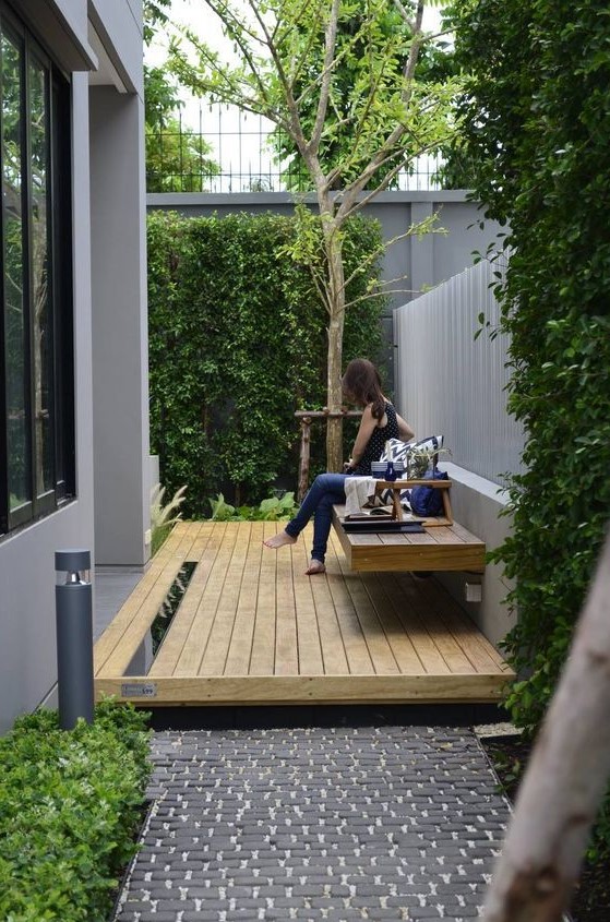 a small modern backyard with a deck and a floating bench plus greenery walls and a tree for relaxing outside