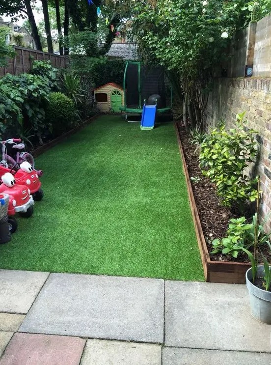 a small walled backyard turned into a kids' entertainment zone with a kid house, some cars and other stuff and covered with artificial turf