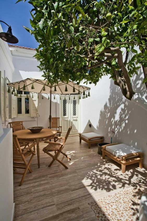 a small yet cool patio done Mediterranean style with a deck, a wooden dining set, a couple of seats and a living tree