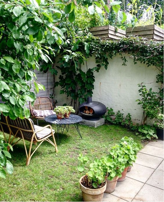 a small yet cozy backyard with rattan furniture, a marble top table, a little hearth and a green lawn