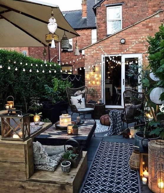 a small yet stylish backyard space with a wooden deck, lots of greenery, lights, candles and simple wooden furniture
