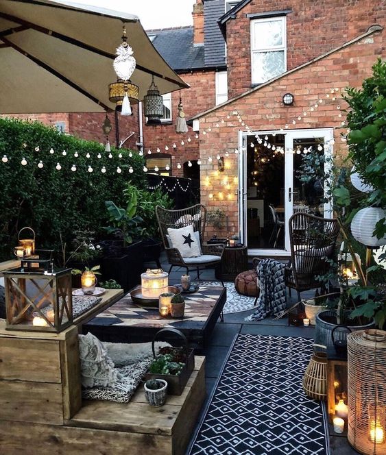 a small yet stylish backyard space with a wooden deck, lots of greenery, lights, candles and simple wooden furniture