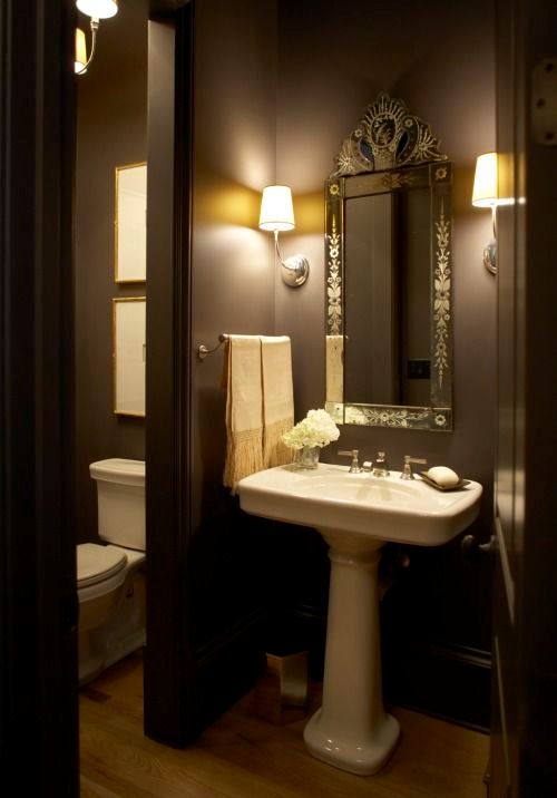 a stylish brown bathroom with a vintage mirror, a free-standing sink and vintage fixtures and lights