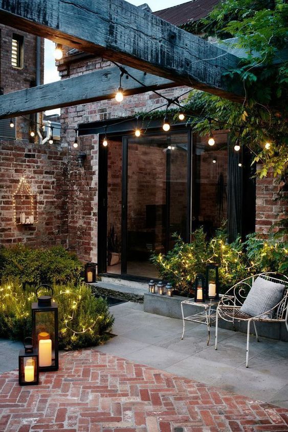 a tiny chic backyard clad with concrete and bricks, with greenery and lights and candle lanterns looks inviting