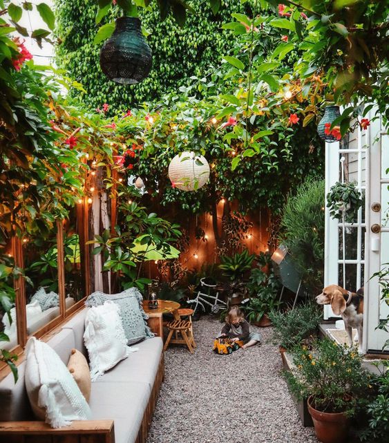 a very cozy small backyard with lots of greenery and blooms, lights, paper lamps and some comfy furniture
