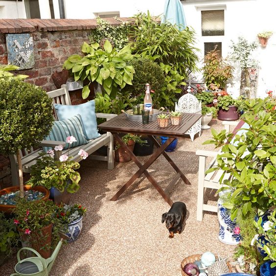 a welcoming backyard with a some wooden folding furniture, potted plants and blooms and bold pillows