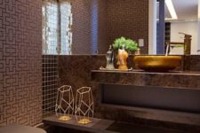 an elegant brown bathroom with printed walls, a brown stone vanity and touches of gold for a glam look