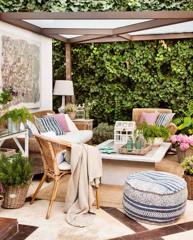 an outdoor living room with rattan furniture, a coffee table, printed pillows and poufs, potted plants and greenery