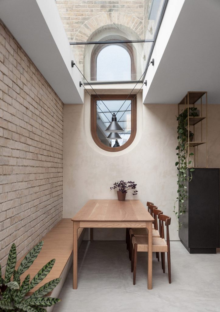 The dining space has a skylight, a built-in bench, a table and woven table plus lots of greenery around