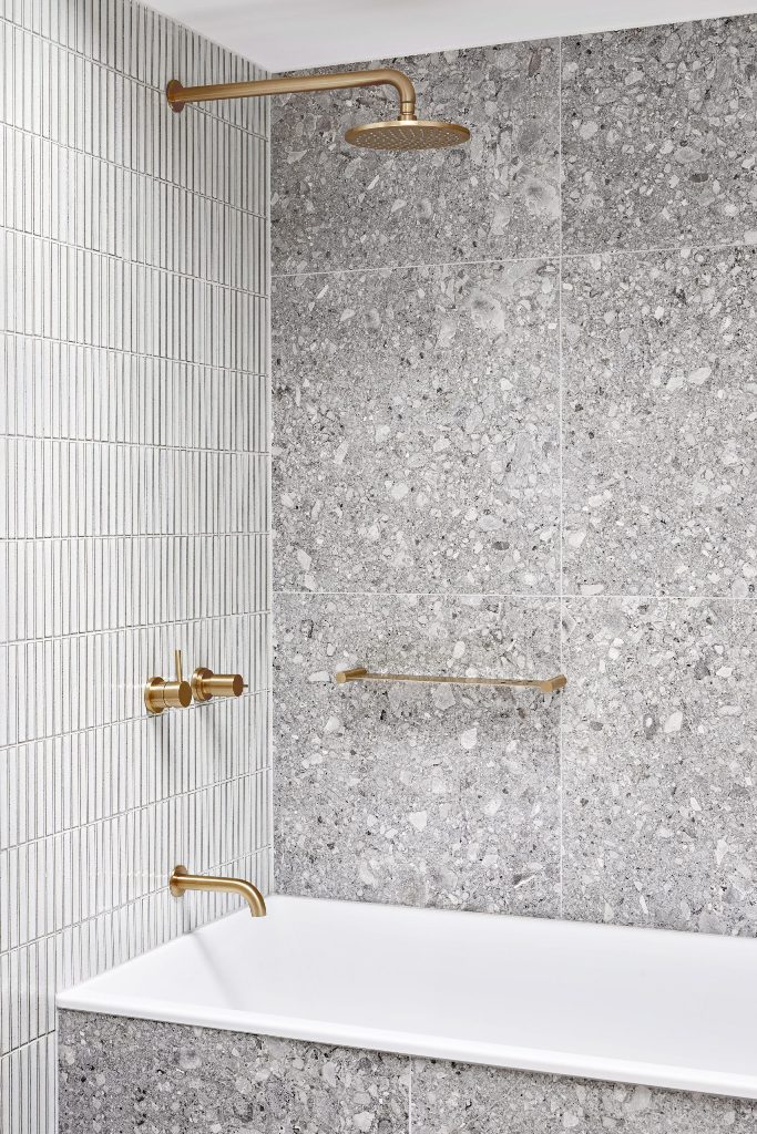bathroom with stone and skinny tiles mixed together The bathroom is clad with grey stone and white skinny tiles and is accented with gold fixtures