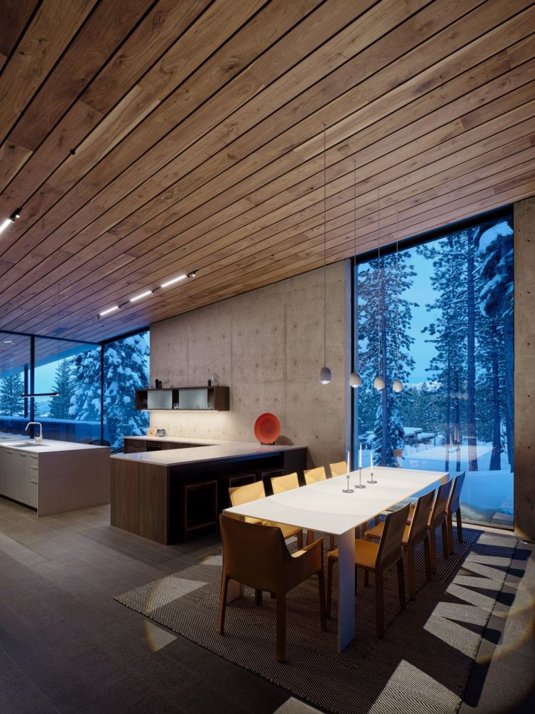 The kitchen and dining area share a large open space with a wooden ceiling, concrete walls and full height windows