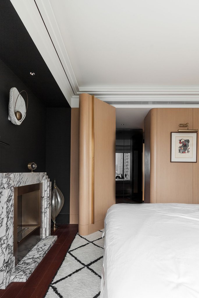 The master bedroom is done with neutral wooden panels, a marble fireplace and a black accent wall