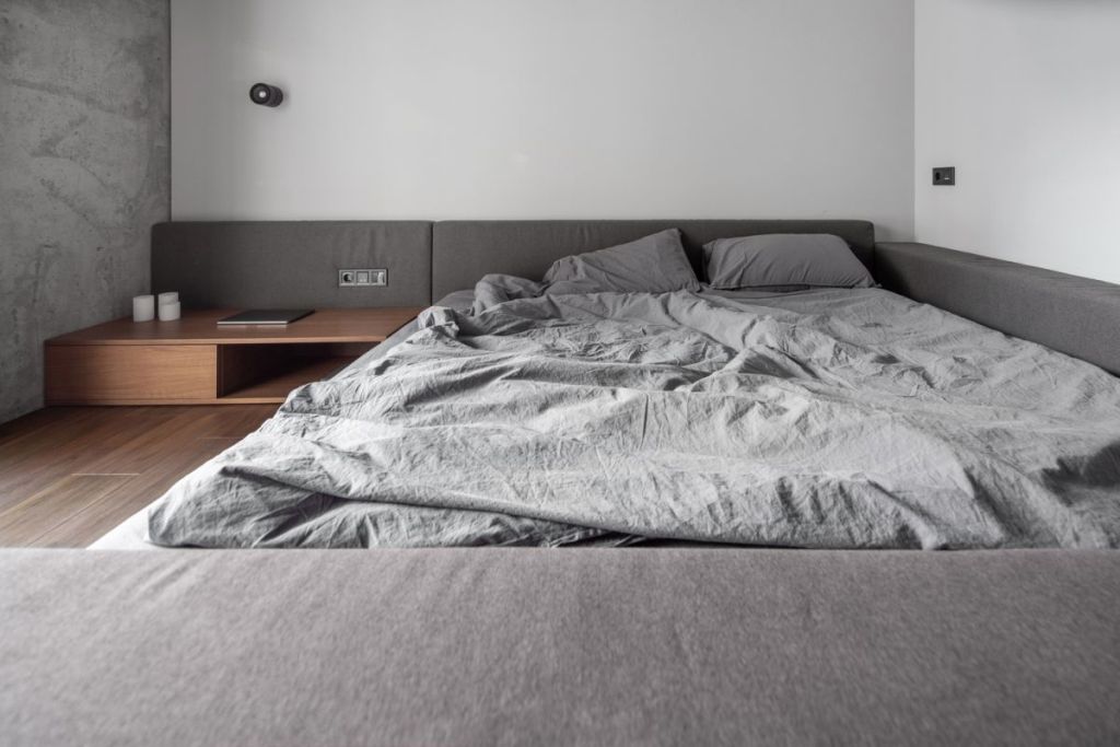 The bedroom is very minimal, done in white and grey, with stained wooden items