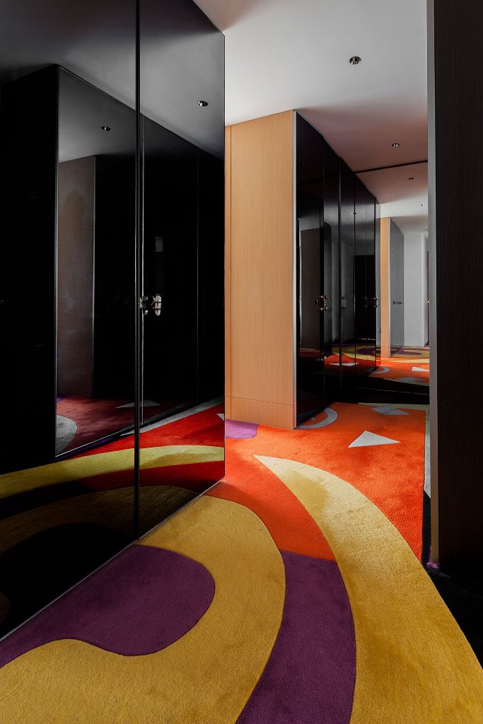 The hallway is colorful, with black shiny doors of wardrobes and colorful rugs
