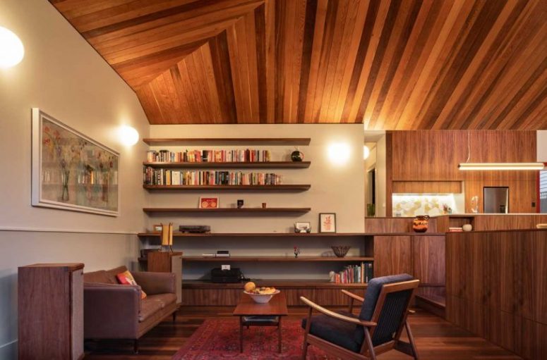 The living room shows off cool floating shelves that echo with the wooden clad ceiling