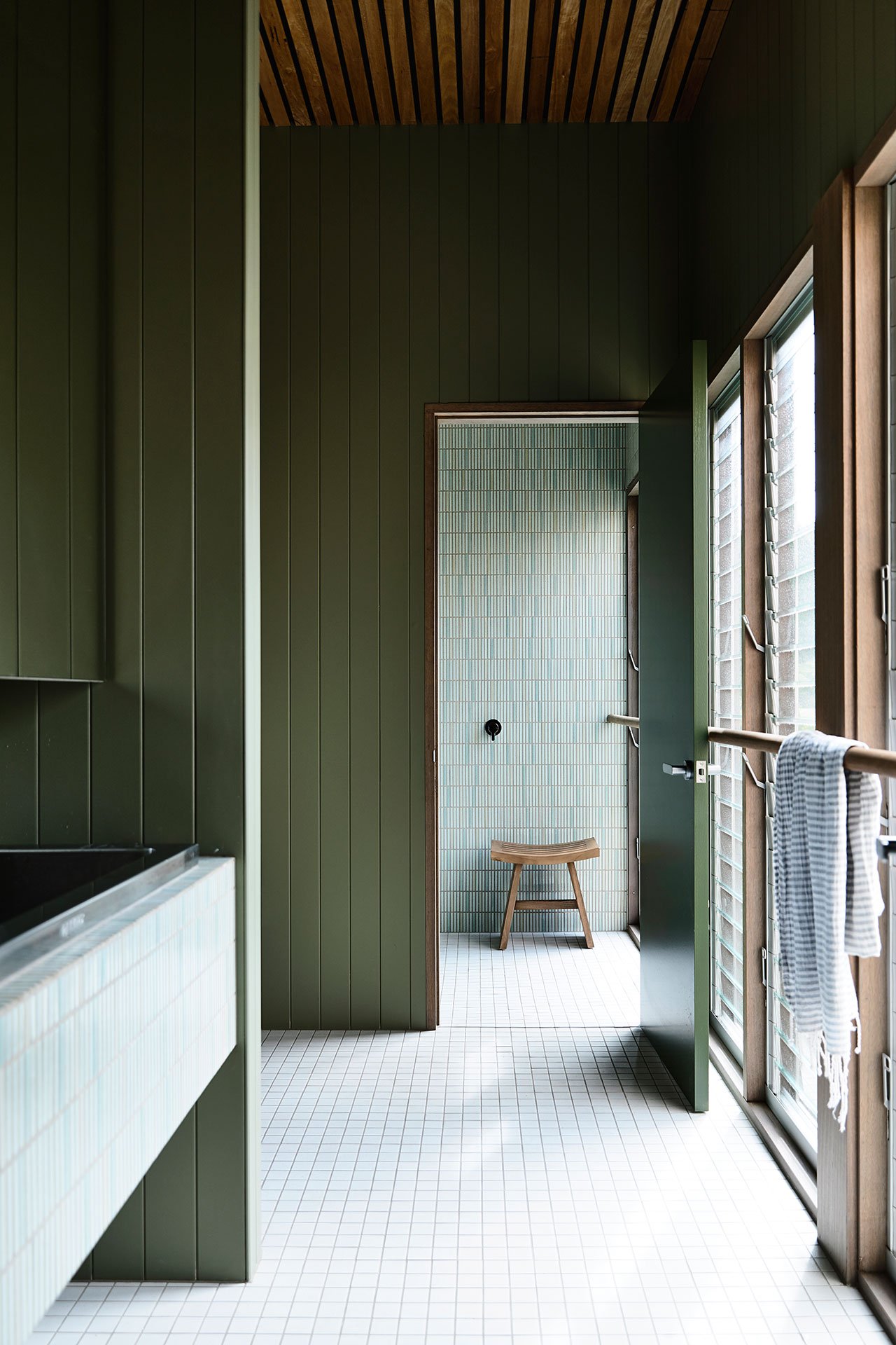 Another bathroom shows off neutral and green tiles that match sage green wood