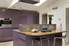 a minimalist purple kitchen with a large island with a wooden dining space and skylights to light it up