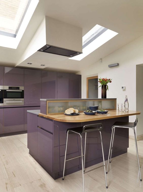 a minimalist purple kitchen with a large island with a wooden dining space and skylights to light it up