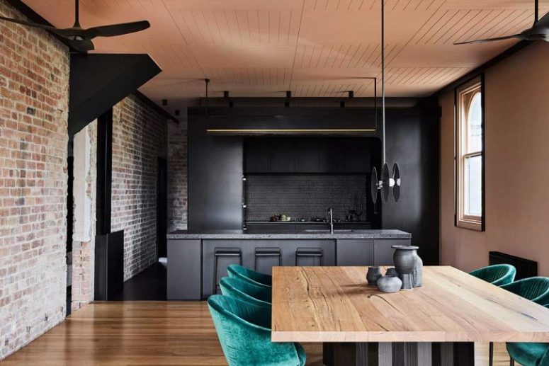 The kitchen and dining room are united, they feature exposed brick, blackened metal and stone and emerald velvet chairs soften the look The kitchen and dining room are united, they feature exposed brick, blackened metal and stone and emerald velvet chairs soften the look