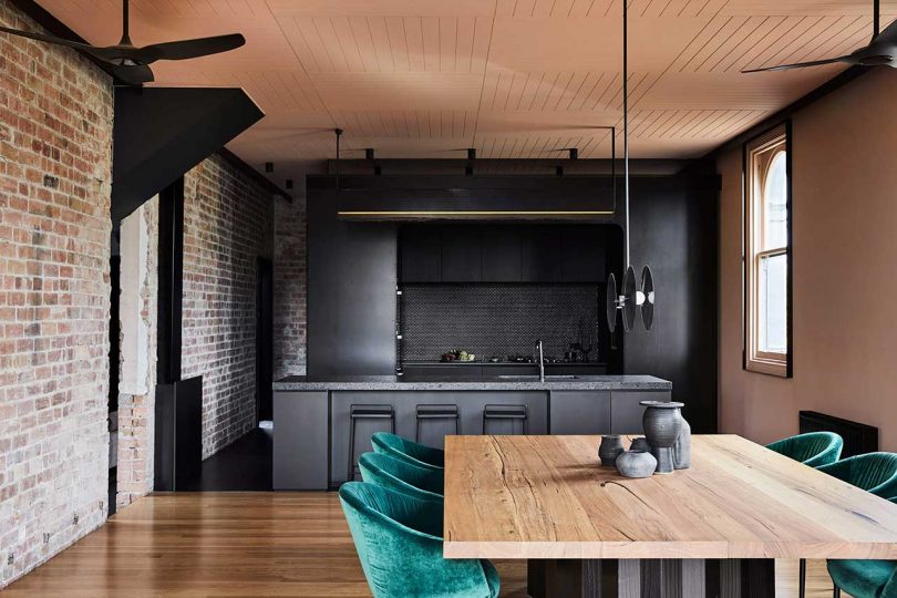 The kitchen and dining room are united, they feature exposed brick, blackened metal and stone and emerald velvet chairs soften the look
