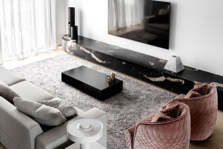 The living room is done with grey furniture, a black marble slba, pink velvet chairs and a fluffy rug and looks exquisite