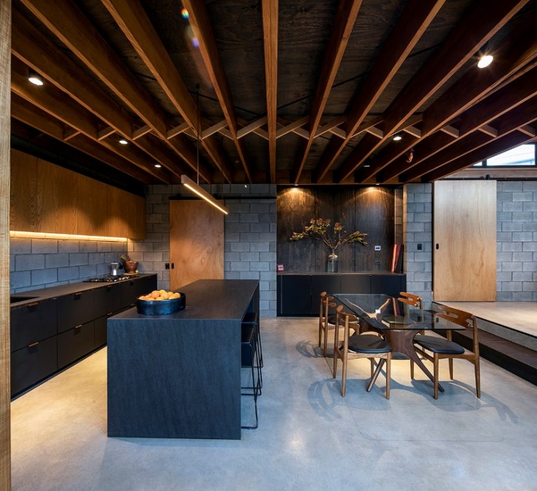 The kitchen is done with concrete, light stained and matte black furniture, a black kitchen island and the dining space features a beautiful glass table The kitchen is done with concrete, light stained and matte black furniture, a black kitchen island and the dining space features a beautiful glass table