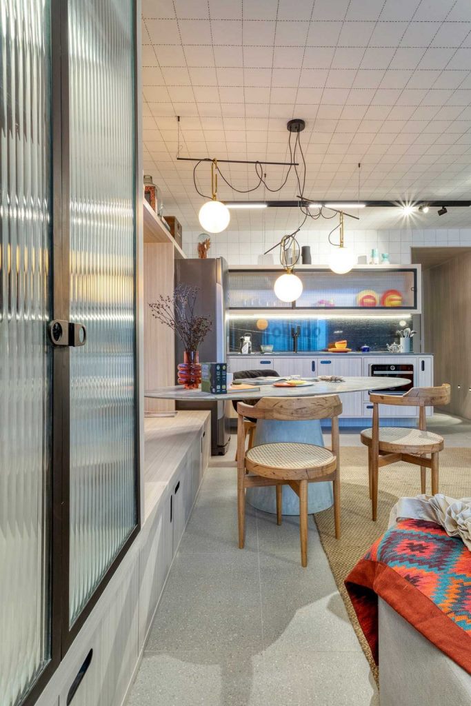 The kitchen is light colored, with a black marble backsplash, the marble top table is standing next to a large storage unit that doubles as a bench The kitchen is light-colored, with a black marble backsplash, the marble top table is standing next to a large storage unit that doubles as a bench