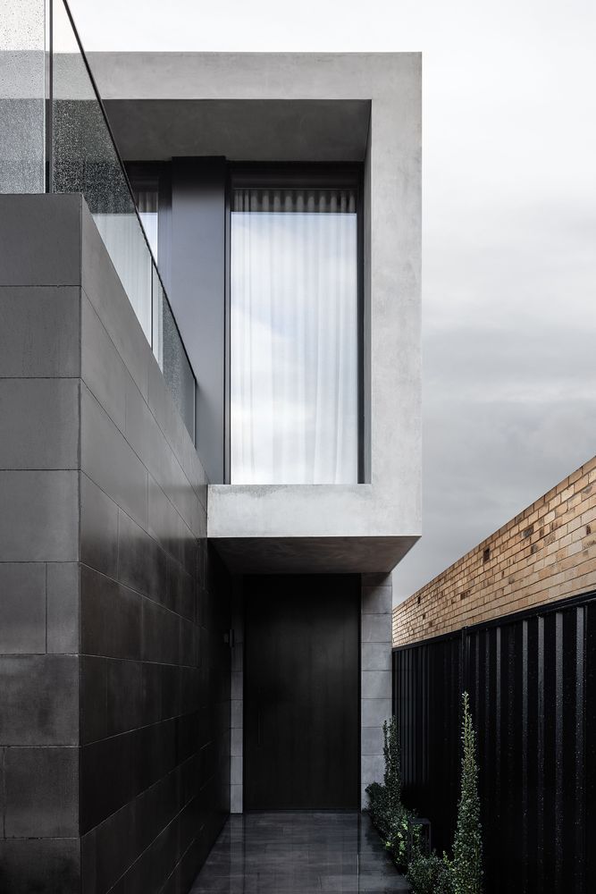 The entrance is framed by a black accent wall and a fence which contrast with the light gray exterior walls