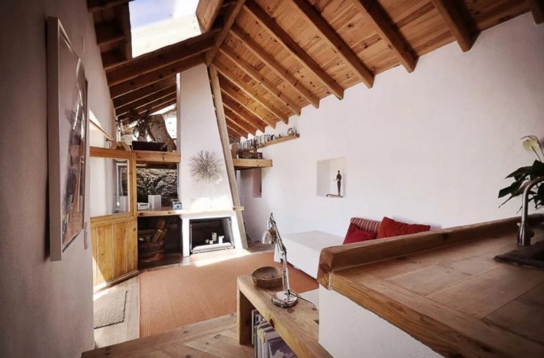 The living room features a fireplace with candles, some simple furniture and a gorgeous wooden ceiling with beams and a skylight