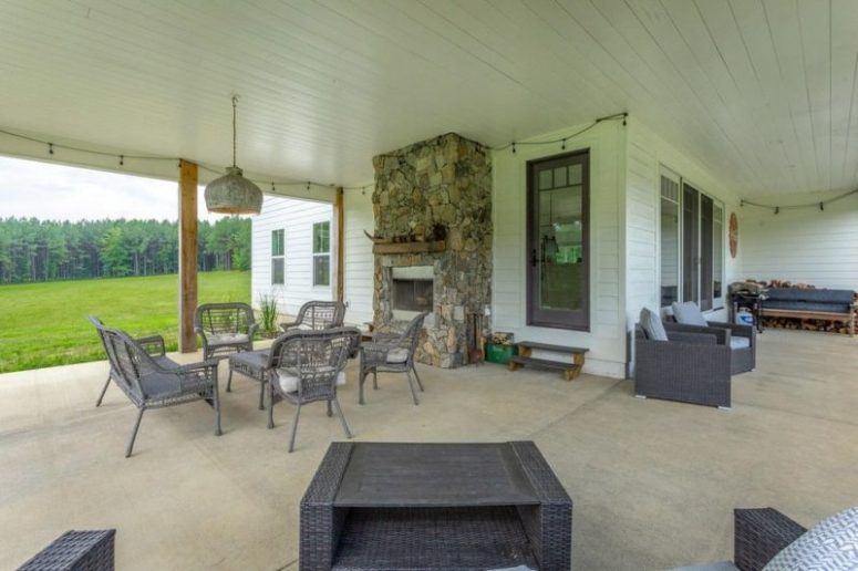 A large covered patio features a stone fire[;ace and woven furniture