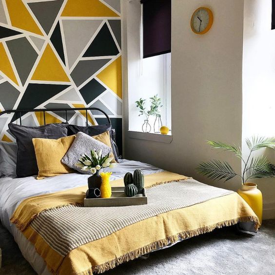 a bold modern bedroom with dove grey walls, a black forged bed, grey and yellow bedding and a geometric grey and mustard wall