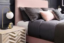 a chic bedroom with black paneling, a pink bed, black and pink bedding and chevron nightstands plus touches of gold