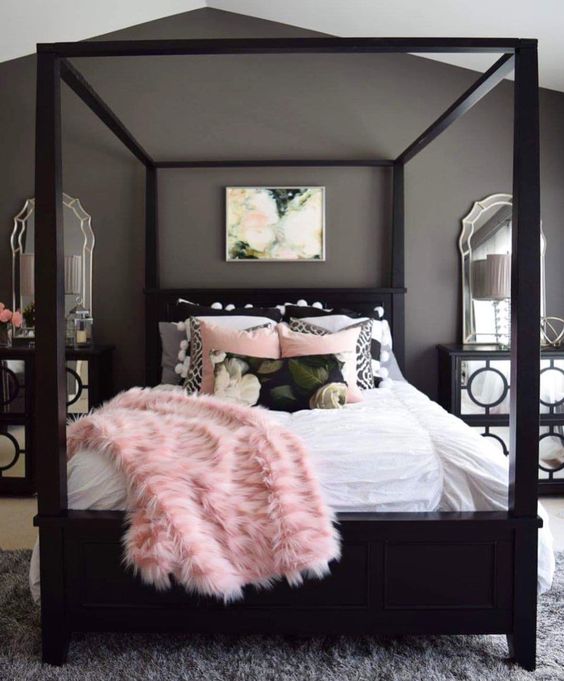 a chic grey bedroom with black furniture, mirrored nightstands, blush and black bedding and layered rugs