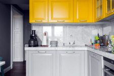 a chic modern kitchen with dove grey and sunny yellow cabinets, a white marble backsplash and countertops plus a tile floor