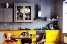 a contrasting and moody kitchen with grey walls and a ceiling, upper cabinets and lower yellow ones, mismatching chairs