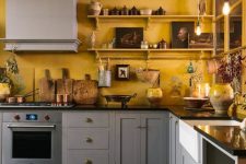 a cozy eclectic kitchen with warm yellow walls and grey cabinets, black countertops and artworks on the shelves