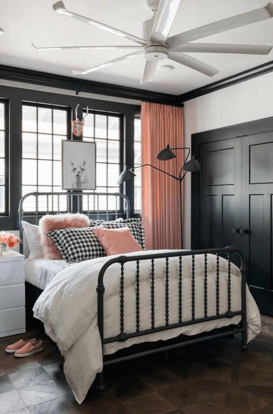 a cute pink, black and white bedroom with black paneling, a forged bed, pink curtains and pillows for a chic look