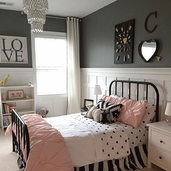 a glam bedroom with black walls, white paneling, a black bed, pink and black bedding, a crystal chandelier and hearts