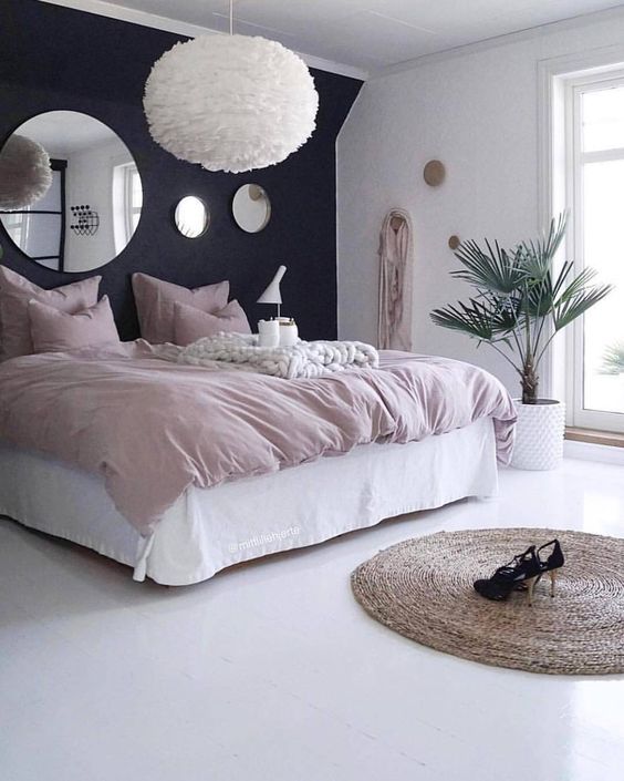 a modern yet romantic bedroom with a black accent wall, white furniture and a fluffy pendant lamp plus blush bedding